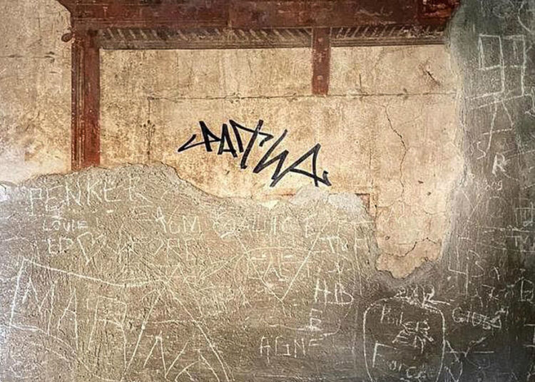 Turista firma con marcador permanente en la pared de una antigua ciudad romana